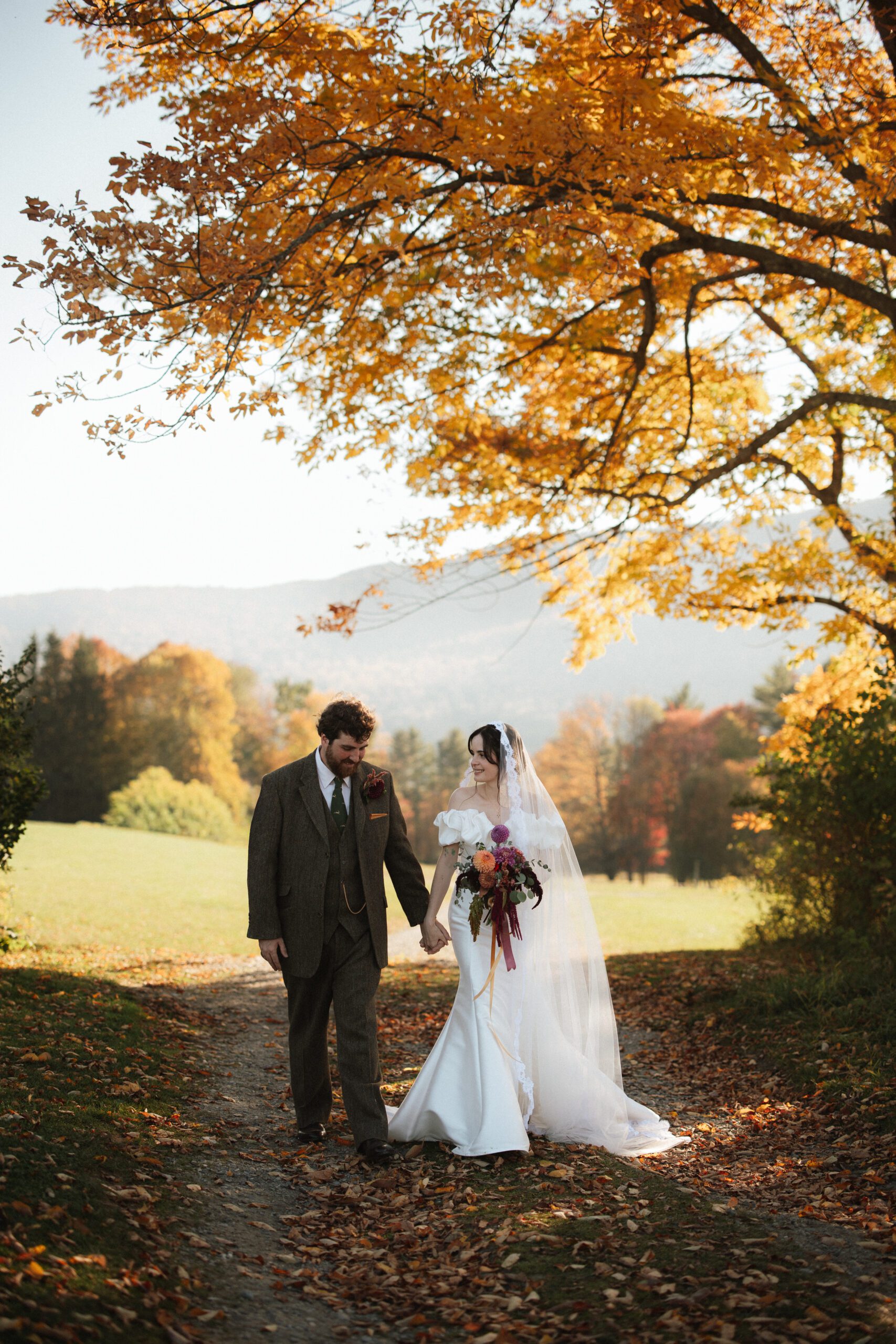 Bride and groom walking hand in hand during a fall Trapp Family Lodge wedding in Stowe, Vermont with golden autumn foliage and mountain views.